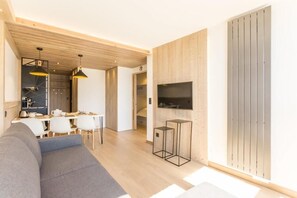 A modern living room with a sofa, dining area, and a TV mounted on a wooden wall.