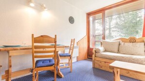 Una habitación acogedora con una mesa de madera, dos sillas, un sofá y un ventanal con vistas a árboles.