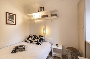Ein Schlafzimmer mit Bett, Nachttisch, Ablagefläche und einer Wandleuchte sowie einem Bild an der Wand.