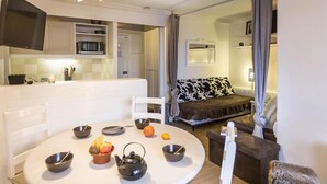 Una sala de estar moderna con una mesa de comedor blanca para cuatro personas, un sofá con funda estampada en blanco y negro, y un televisor montado en la pared.