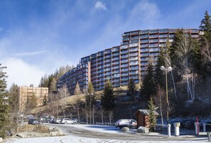 Um hotel com vários andares e design arquitetônico moderno, situado numa área arborizada e com um parque de estacionamento.