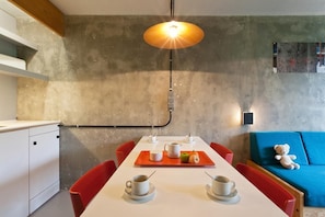 Een moderne eethoek met een witte tafel, rode stoelen en een blauwe bank met een teddybeer.