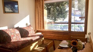 A cozy room with a wooden sofa, a dining table with a vase of flowers, and a window with a view of trees and a balcony. - 10m from ski slopes, 11st floor, balcony, tv, 28m², Les Arcs (Les Arcs)