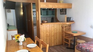 A compact room with a wooden dining table set for two, a small kitchen area with a wooden counter, and a single bed with a patterned blanket. - 10m from ski slopes, 11st floor, balcony, tv, 28m², Les Arcs (Les Arcs)