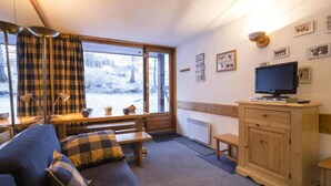 A cozy room with a sofa, a wooden bench, a television, and a window with a view of a snowy landscape. - 10m from ski slopes, 8th floor, terrace, tv, 27m², Les Arcs (Les Arcs)