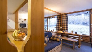 A cozy cabin interior with a wooden bench, a sofa, a dining table, and a large window with plaid curtains. - 10m from ski slopes, 8th floor, terrace, tv, 27m², Les Arcs (Les Arcs)