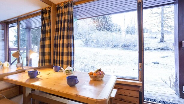 A cozy room with a wooden table, a bench, and a window with plaid curtains. Outside, there's a snowy landscape with trees. - 10m from ski slopes, 8th floor, terrace, tv, 27m², Les Arcs (Les Arcs)