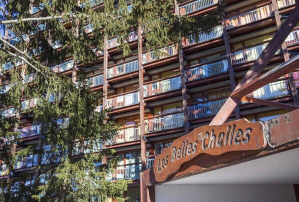Un edificio de varios pisos con balcones, un cartel que dice "Les Belles Challes" y árboles circundantes.