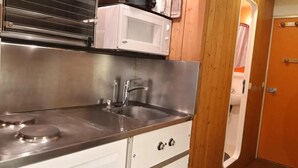 Een kleine keuken met een RVS-gootsteen, een magnetron en een fornuis.