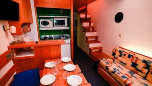 A compact kitchen with a microwave and stove, a dining table set with plates and glasses, and a patterned sofa.