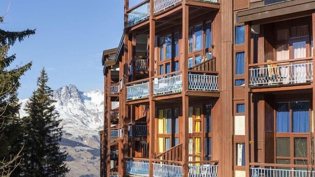A multi-story wooden building with balconies, set against a snowy mountain backdrop.