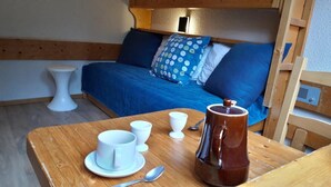 A cozy room with a bed, a wooden table with cups and a coffee pot, and a small white stool. - 50m from resort center, 13rd floor, 13m², Les Arcs (Les Arcs)