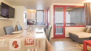 Ein Essbereich mit Tisch für vier Personen, einem an der Wand montierten Fernseher und einer Glasschiebetür, die auf einen Balkon führt.