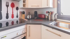 Eine kompakte Küche mit Herd, Backofen und Spüle. Auf der Arbeitsplatte befinden sich Geschirr und ein Toaster.