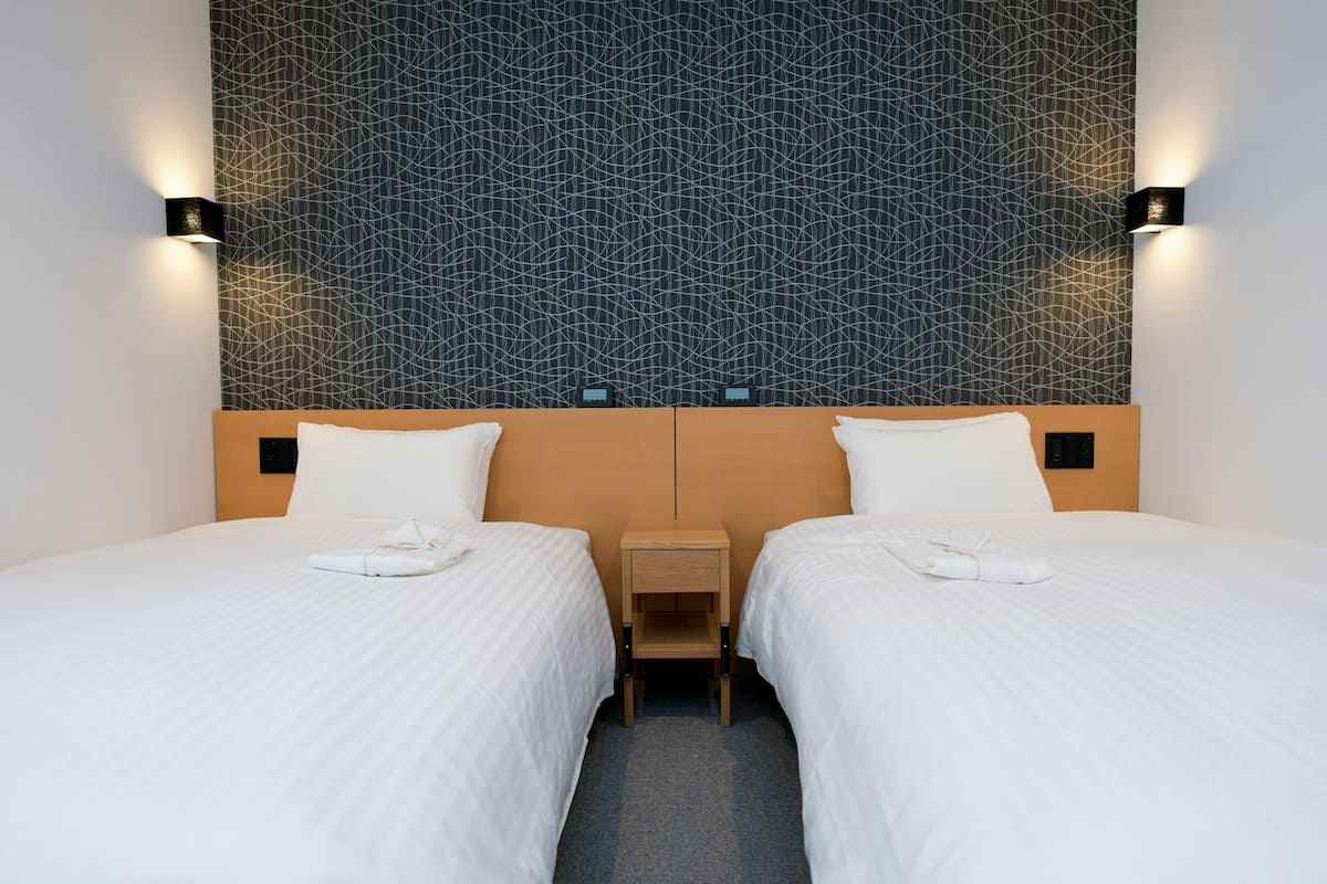 A hotel room with two beds, a wooden headboard, and a patterned wall.