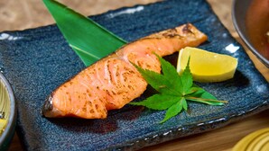 Une assiette contenant du saumon grillé, un quartier de citron et une garniture de feuilles vertes.