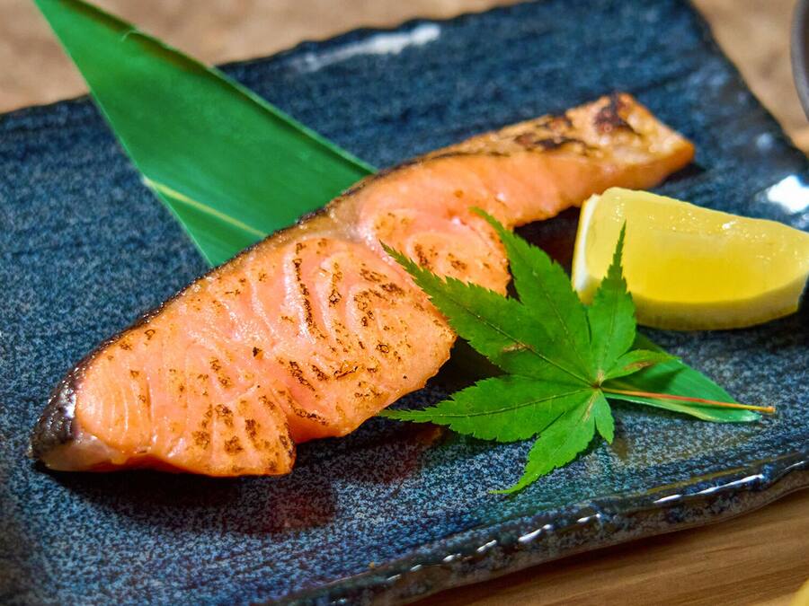 A plate with grilled salmon, lemon, and a green leaf garnish.