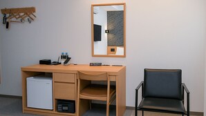 Un petit espace de bureau comprenant un bureau en bois, une chaise noire, un petit réfrigérateur et un miroir accroché au mur.