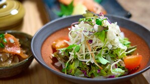 A bowl of salad with various greens and vegetables, a small bowl of sauce, and a piece of meat on the side. - You Style Hotel Hakata (Fukuoka)
