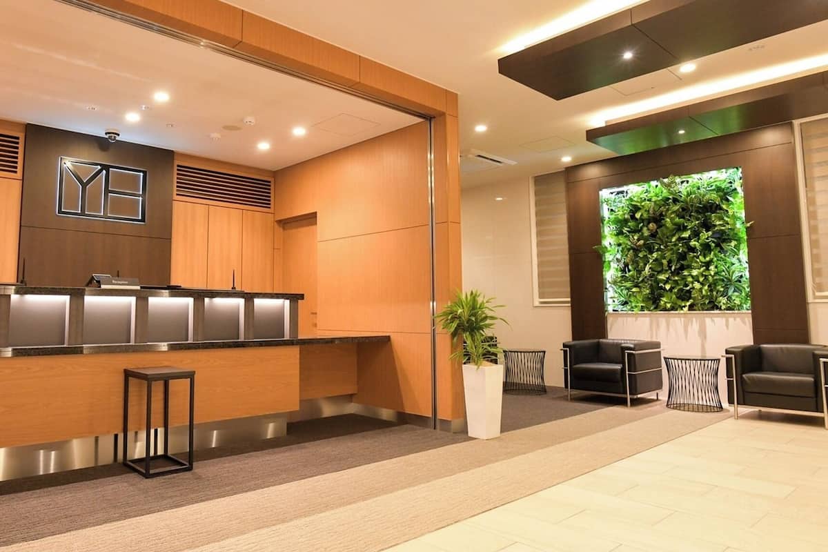A reception area with a wooden reception desk, a reception sign, a potted plant, and a seating area with two chairs and a small table.