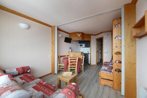 A cozy room with a wooden sofa, a small table, and a kitchen area with a microwave and a TV. - 10m from ski slopes, view mountain, balcony, tv, 26m², La Plagne (Aime)