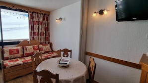 A cozy room with a wooden bench, a round table, and a TV mounted on the wall. - 10m from ski slopes, view ski slopes, balcony, tv, 26m², La Plagne (Aime)
