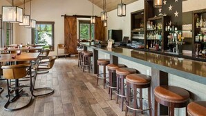 Un espace bar doté d’un plancher en bois, de tabourets de bar et d’un comptoir où sont exposées diverses bouteilles et verres.