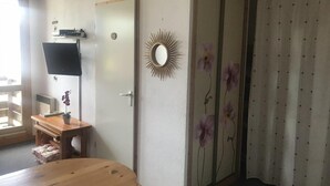 Een kamer met een houten tafel, een klein bureau met een computer, een spiegel en een schuifdeur met bloemenbehang.