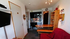 Een knus woongedeelte met een rode bank, houten tafels, een televisie en een keukenhoek.