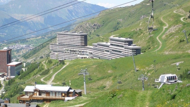 A hotel with multiple buildings, a ski lift, and a mountainous backdrop.