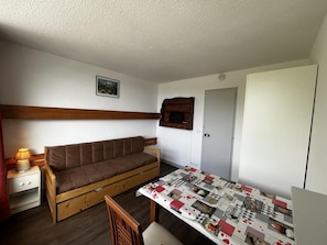 A compact room with a sofa, a small table with a quilt, a cabinet, and a door.