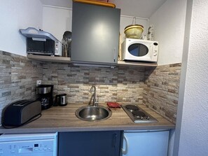 Cocina compacta con microondas integrado, pileta de acero inoxidable, cafetera y tostadora.