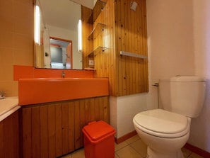 A bathroom with a wooden panel wall, a white toilet, and an orange sink.