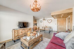 Una sala de estar moderna con un mueble de televisión de madera, un sofá rojo, una zona de comedor con un adorno de corazón en la pared y una cocina al fondo.