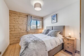 Une chambre avec un mur en bois, un lit avec une literie blanche, une table de chevet avec une lampe et une fenêtre avec des rideaux.