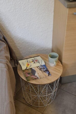 Ein kleiner runder Tisch mit einem Gestell aus Metalldraht, ein Buch und eine Tasse.