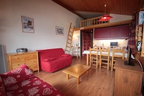 A cozy room with a red sofa, wooden coffee table, and a loft area with a desk and chair.