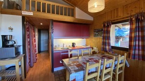 Ein gemütliches Blockhauss-Interieur mit einem Holzesstisch, roten Küchenschränken und einem Schlafzimmer im oberen Bereich mit Etagenbett.