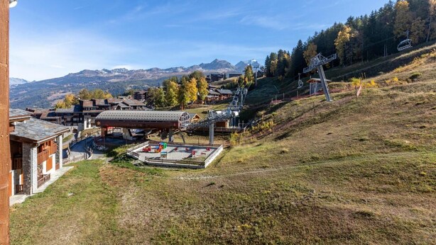 A ski resort with a ski lift, buildings, and a mountainous backdrop.