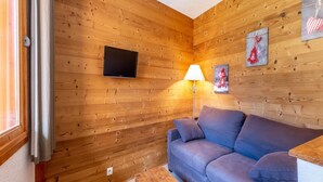 A cozy room with wooden walls, a blue sofa, a wooden table, and a TV mounted on the wall.