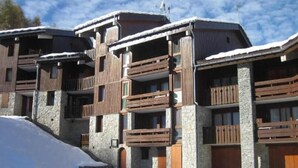 A multi-story hotel with stone and wood exterior, balconies, and a snowy landscape.