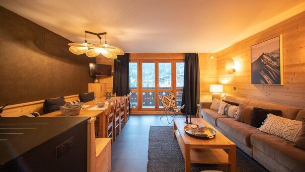 Une chambre confortable, aménagée dans le style d’un chalet, avec un coin repas, un canapé et une grande fenêtre offrant une vue sur les montagnes.