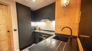 Une cuisine moderne avec des meubles de couleur sombre, un plan de travail en acier inoxydable et un mur d’accent en bois.