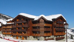 Un chalet en bois à plusieurs étages, doté de balcons, situé dans une région montagneuse enneigée.