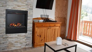 Una sala de estar con pared de piedra, chimenea, un mueble de madera, televisor montado en la pared y puerta corrediza de vidrio al exterior.