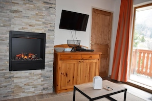 Una sala de estar con pared de piedra, chimenea, un mueble de madera, televisor montado en la pared y puerta corrediza de vidrio al exterior.