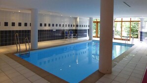 Una piscina interior con paredes de azulejos, agua azul cristalina y algunas sillas cerca.