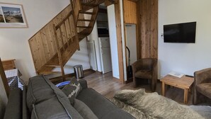 Ein kompakter Wohnbereich mit einer Couch, zwei Sesseln, einer Holztreppe, einer Küchenzeile und einem angebrachten Fernseher.