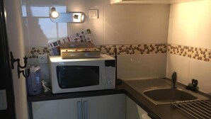 A compact kitchen with a microwave, a sink, and a dishwasher. There is a small trash bin and a cabinet with a tiled backsplash. - 100m from resort center, 1st floor, view mountain, balcony, tv, 27m², Gourette (Eaux-Bonnes)
