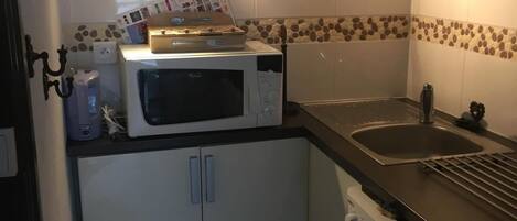 A compact kitchen with a microwave, a sink, and a dishwasher. There is a small trash bin and a cabinet with a tiled backsplash.